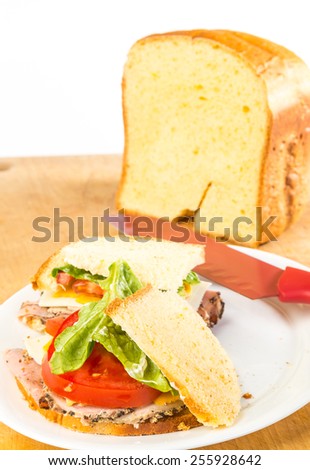 Fresh loaf of homemade cheese bread in background of roast beef and pork tenderloin sandwich against white background.  Vertical format with copy space.
