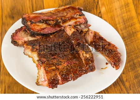 Slab of baby back ribs on white platter with sliced beef brisket against rustic wood table background.