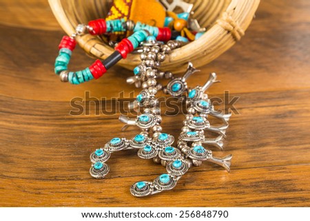 Turquoise and coral and silver Native American jewelry spilling from vintage wicker basket onto old wooden board floor.