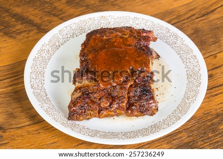 Half slab of leftover Barbecue baby back ribs reheated in microwave and served on rustic wooden tabletop.