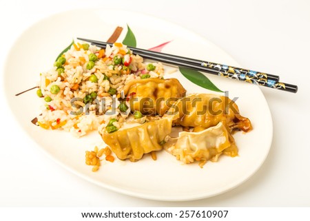 Chinese pot stickers with rice and vegetables on Oriental design plate with chopsticks.