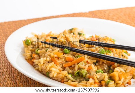 Plate of chicken fried rice with chopsticks on white plate against bamboo place mat.