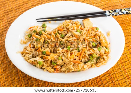 Plate of chicken fried rice with chopsticks on white plate against bamboo place mat.