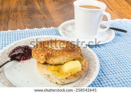 Melting Butter on Sesame and Poppy Seed Bagel with jam and coffee.  Country kitchen setting with blue gingham place mat and rustic wood background.