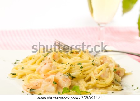 Selective focus on shrimp alfredo dinner with soft focus on glass of white wine in background.  Horizontal with white background and copy space.