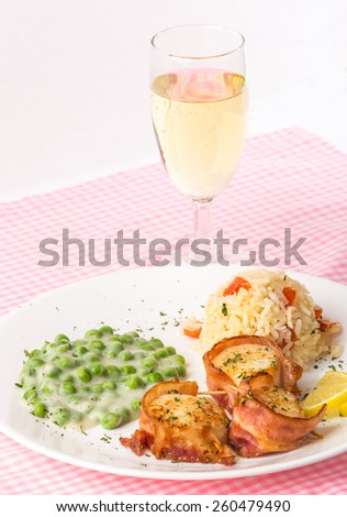 Bacon-wrapped scallops with rice and creamed sweet peas with stemmed glass of Mosel Riesling wine.  Vertical with bright light from upper right.