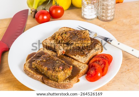 Making a meatloaf sandwich on whole grain toast smothered in brown gravy with sliced tomatoes.