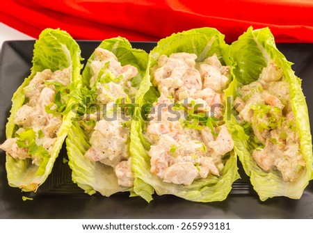 Four spicy shrimp salad wraps in lettuce leaf on black serving platter with bright red napkin.