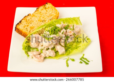 Spicy seasoning on shrimp salad in lettuce leaf wrap with slice of jalapeno cheese loaf on bright red tablecloth background.