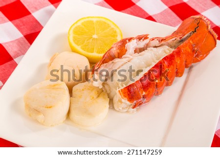 Three poached scallops on square white plate with steamed lobster tail with shell split and large slice of lemon.  Red Plaid Tablecloth background.