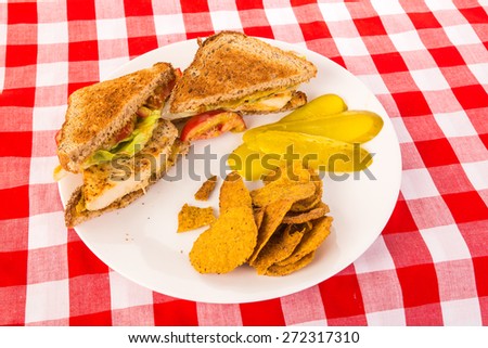 Sliced chicken breast on whole wheat toast with honey mustard and tomatoes.  Served with sweet potato chips and pickle slices.