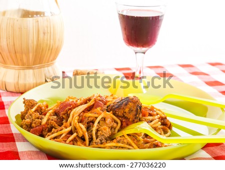 Strong light from right rear on spaghetti and meatballs on plastic picnic dishes with Chianti in glass and wicker-wrapped bottle.
