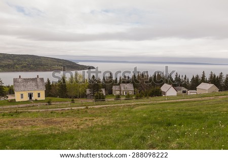 Looking across pasture at historic Gaelic village and living history museum in Nova Scotia with Bay of Fundy in Background.