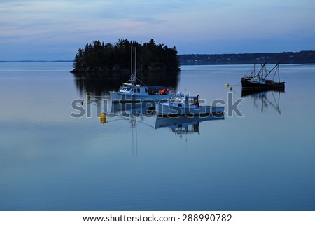 Fishing boats reflecting in calm water of Bay of Fundy near Lubec, Maine in evening light.