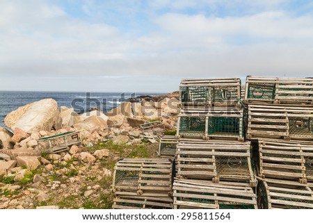 Old fashioned wooden lobster pots stored by shoreline with blue waters of Bay of Fundy and soft clouds as background.