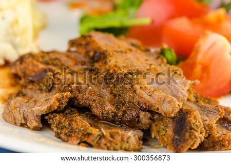 Closeup of flank steak cooked in jerk sauce and served with mashed potatoes and salad.