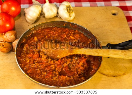 Tomato and meat sauce in skillet on wooden cutting board surrounded by ingredients.  Overhead View