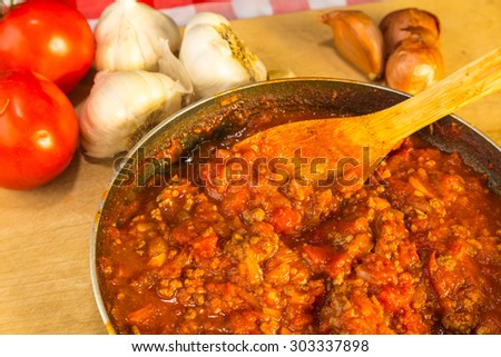 Closeup overhead view of meat and tomato spaghetti sauce in skillet on wooden cutting board surrounded by fresh ingredients.