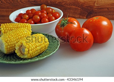Boiled corn on the cob, vine-ripened tomatoes, and a bowl of cherry tomatoes on a kitchen counter top.
