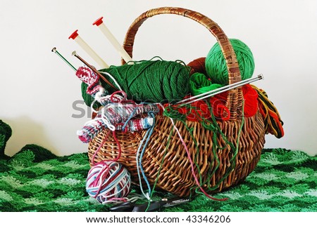 Closeup of handmade wicker basket filled with yarn, thread, knitting needles and sewing supplies setting on a knitted  green afghan. Isolated on neutral background.