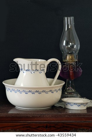 Still life with an antique wash basin and pitcher on marble-top wash stand isolated on black.  Kerosene lamp and soap dish included.