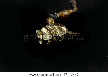 Closeup of a gold-plated armadillo charm at the end of a beaded string and isolated on harsh black background.