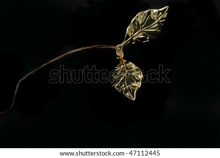 Closeup of two gold leaves on a string that is used for a book marker.  Isolated on harsh black background.