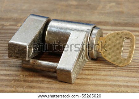 Used and rusty trailer lock with key inserted and laying on rustic old wooden work bench.  Lock is used to secure a trailer tongue to its trailer hitch.