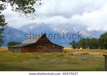 Snow over the Tetons with heavy clouds and soft patches of light on Moulton Barn on Mormon Row in Jackson Hole in Grand Teton National Park, Wyoming.