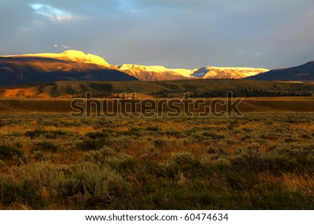 Soft, warm light filtered through storm clouds over Tetons gives golden glow to Jackson Hole in Grand Teton National Park, Wyoming.  Snow blankets Gros Ventre Mountain Range east of Jackson Hole.