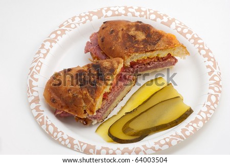 Closeup of Hot Roast Beef Sandwich on baked Garlic Bread with sliced bread and butter pickle served on paper plate against white background.