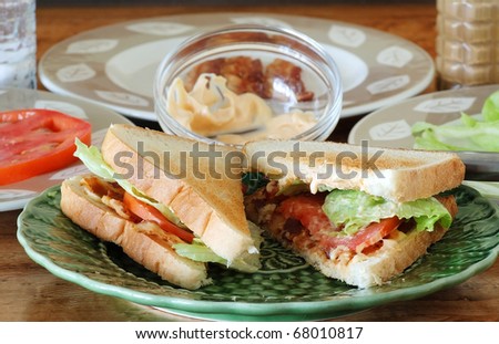 Bacon, Lettuce and Tomato sandwich on toast with chipotle mayonnaise, surrounded by ingredients and setting on wooden counter top.