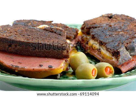 Grilled cheese and fried jalapeno bologna sandwich on pumpernickel bread, served with stuffed olives on green plate.