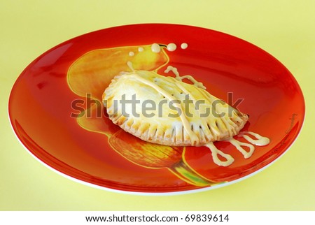 Panamanian style meat-filled empanada on bright red and orange plate drizzled with honey mustard.