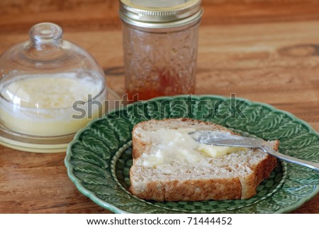 Slice of buttered homemade bread, with jar of homemade peach jelly and antique butter dish filled with rendered butter.