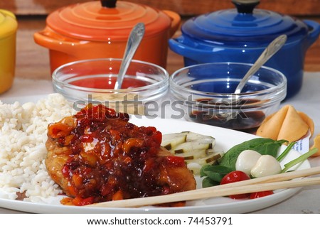 Chicken in colorful orange sauce served with rice, soy sauce and hot mustard and chop sticks.
