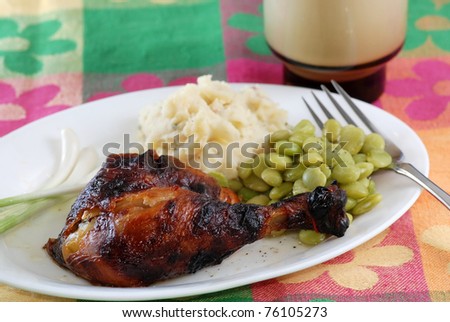 Roast Chicken Leg and thigh on white plate with mashed potatoes, lima beans and glass of milk on colorful table cloth.