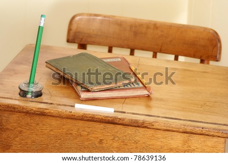 Closeup of vintage school desk and chair against pale yellow background with old books, pencil, inkwell and stick of chalk.