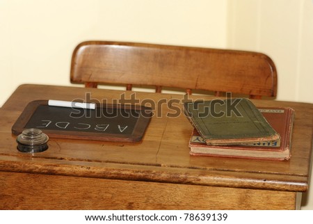 Closeup of antique school desk and chair with small chalk board, some old books and an ink well against pale yellow background.