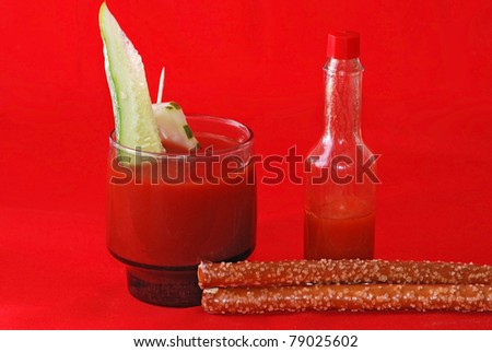 Mixed drink with tomato juice and bottle of hot sauce with salty pretzels and piece of cucumber in drink glass. Dramatic use of red on red.