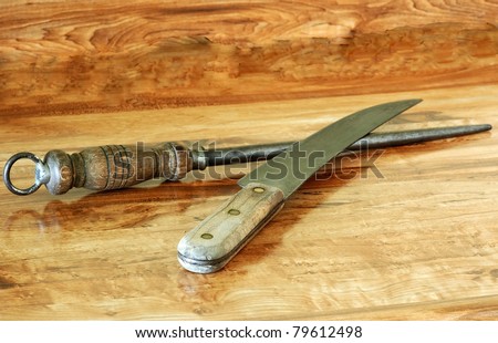 Old butcher knife and antique sharpening steel laying on wooden cutting block.