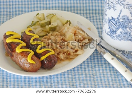 Grilled bratwurst on plate with fried cabbage and cucumber salad sitting on blue and white place mat with Bavarian Bier Stein.