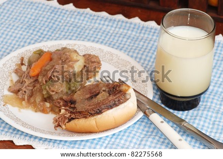 Pot roast spread over toasted bun; roast beef, vegetables and gravy with knife and fork on blue gingham place mat with glass of cold milk.