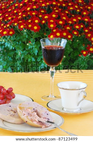 Blueberry bagel with strawberry butter on fine china served with coffee, juice, and fruit with fresh chrysanthemum in background.