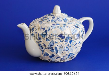 Handcrafted teapot of broken pieces of ceramic and porcelain glass.  Blue and white and shown on blue background.