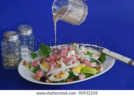 Fat Free Poppy Seed dressing pouring over ham and egg salad with blue background.