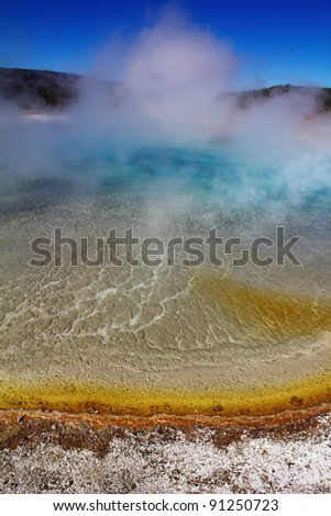 Steam rising from vibrantly colored water of thermal pool in Midway Geyser Basin area of Yellowstone National Park in Wyoming