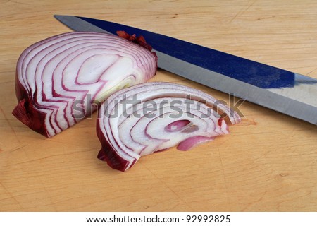 Slices of red onion on wooden cutting board with blade of butcher knife.