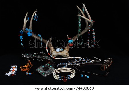 Assortment of handcrafted Native American turquoise and silver jewelry and beaded accessories hanging from deer antler all against black background.