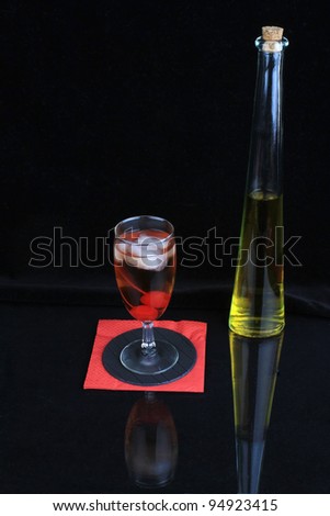 Whiskey sour with two cherries reflecting on shiny bar surface with bottle in background